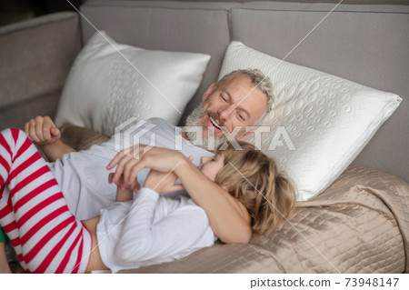 Man hugging child lying on bed Man hugging child lying on bed 73948147
