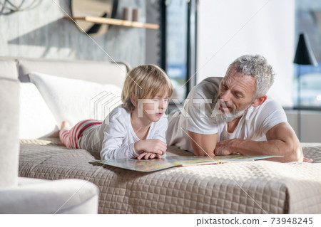Gray-haired man reading children book and child Gray-haired man reading children book and child 73948245