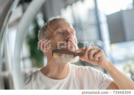 Man styling his beard with a comb 73948309