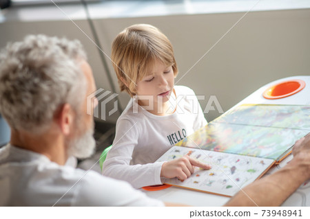 Boy reading an interesting book together with his father Boy reading an interesting book together with his father 73948941
