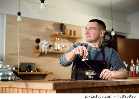 Barista presses ground coffee using tamper in a coffe shop 73950950