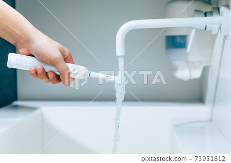 hand holding a toothbrush under flowing water from faucet in a bathroom hand holding a toothbrush under flowing water from faucet in a bathroom 73951812