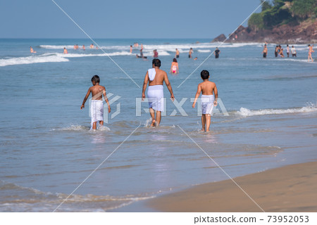 Indian man and kids, all wearing traditional swimming garments, enjoy the sea in Varkala, Kerala. Family vacation in India. Indian man and kids, all wearing traditional swimming garments, enjoy the sea in Varkala, Kerala. Family vacation in India. 73952053