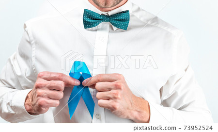 Blue ribbon. Awareness prostate cancer of men health in November. Hipster men in bright shirt, cyan bowtie with blue ribbon in hands on white background. Symbol of oncology affected man. Copy space. Blue ribbon. Awareness prostate cancer of men health in November. Hipster men in bright shirt, cyan bowtie with blue ribbon in hands on white background. Symbol of oncology affected man. Copy space. 73952524