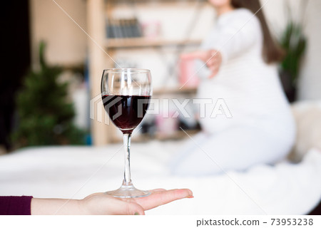 Pregnant woman keeping glass of wine. Future mother drinking alcohol while expecting little baby 73953238