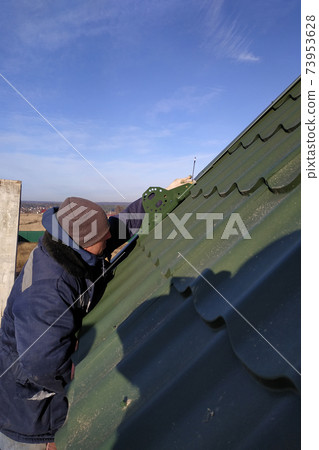 The worker screws the snow retaining elements to the roof with a screwdriver 73953628