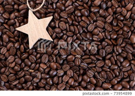 Wooden star lying on coffee beans background Wooden star lying on coffee beans background 73954899