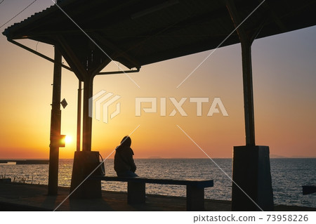 A woman looking at the Seto Inland Sea dyed in the sunset at Shimonada Station on the JR Shikoku Yosan Line A woman looking at the Seto Inland Sea dyed in the sunset at Shimonada Station on the JR Shikoku Yosan Line 73958226