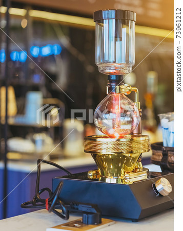 Close up to barista make coffee with Vacuum Pot Syphon Brewer.  Syphon (Siphon) coffee maker brews drink using two chambers where vapor pressure and vacuum produce coffee in cafe. Selective focus. 73961212