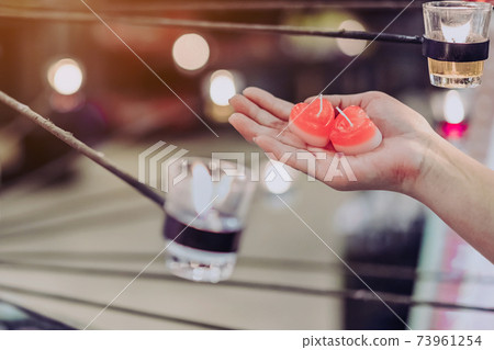 A red heart shaped candle in a woman's hand with candlelight in many small glass cups. A valentine's day background. A red heart shaped candle in a woman's hand with candlelight in many small glass cups. A valentine's day background. 73961254