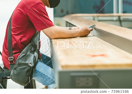 Man using mobile phones for work with blurred image of alternative seating mark for social distance rules distance for one seat from other people to protect from Corona Virus(COVID-19) in foreground 73961586