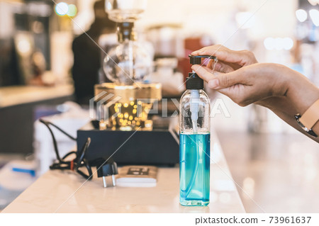 Hands of woman pressed blue alcohol gel bottle to prevent the spreading of the Coronavirus (Covid-19) before entrance to coffee shop. New normal lifestyle. Selective focus on alcohol gel bottle. Hands of woman pressed blue alcohol gel bottle to prevent the spreading of the Coronavirus (Covid-19) before entrance to coffee shop. New normal lifestyle. Selective focus on alcohol gel bottle. 73961637