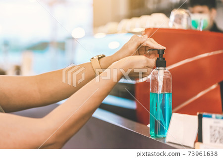 Hands of woman pressed blue alcohol gel bottle to prevent the spreading of the Coronavirus (Covid-19) before entrance to coffee shop. New normal lifestyle. Selective focus on alcohol gel bottle. Hands of woman pressed blue alcohol gel bottle to prevent the spreading of the Coronavirus (Covid-19) before entrance to coffee shop. New normal lifestyle. Selective focus on alcohol gel bottle. 73961638
