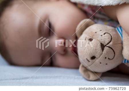 Childhood, care, motherhood, health concepts - Close up Little peace calm infant toddler baby girl sleep resting take deep nap laying hug teddy bear toy on soft warm blanket with close eyes on big bed Childhood, care, motherhood, health concepts - Close up Little peace calm infant toddler baby girl sleep resting take deep nap laying hug teddy bear toy on soft warm blanket with close eyes on big bed 73962720
