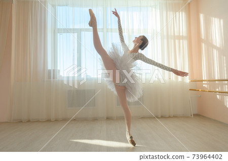 Beautiful ballerina in body and white tutu is training in a dance class. Young flexible dancer posing in pointe shoes. 73964402
