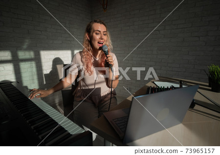 A female blogger sings and plays the live electronic piano. Portrait of a girl recording a song on a web camera and composing on a synthesizer. Online music lessons. Distance learning in quarantine. A female blogger sings and plays the live electronic piano. Portrait of a girl recording a song on a web camera and composing on a synthesizer. Online music lessons. Distance learning in quarantine. 73965157