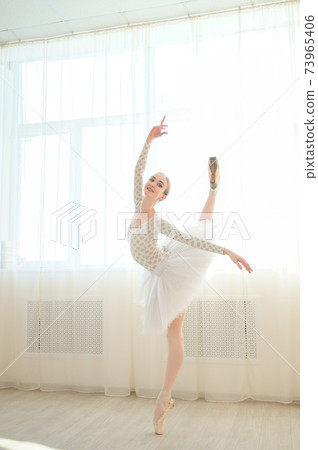 Beautiful ballerina in body and white tutu is training in a dance class. Young flexible dancer posing in pointe shoes. Beautiful ballerina in body and white tutu is training in a dance class. Young flexible dancer posing in pointe shoes. 73965406