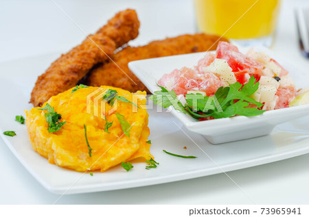 Breaded and herbed chicken breast fillet served with mashed carrots with potatoes  and  tomato salad with onions 73965941
