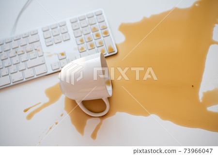Spilled black coffee on a computer keyboard at a white table 73966047