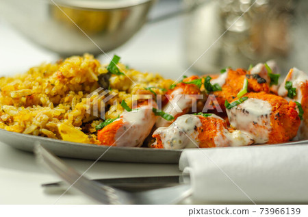 Pieces of cooked marinated chicken breast in an onion and tomato sauce with yogurt and mint and crispy fried onions layered with spiced basmati rice 73966139