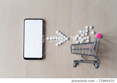 Online pharmacy concept. Buying medicine online over the phone. Delivery of pharmaceuticals. Mini trolley with tablets and smartphone with white blank screen. 73966410