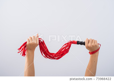 Red leather whip in female hands on a white background. Copy space. Red leather whip in female hands on a white background. Copy space. 73966422