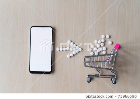Online pharmacy concept. Buying medicine online over the phone. Delivery of pharmaceuticals. Mini trolley with tablets and smartphone with white blank screen. 73966580