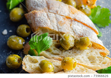 Baguette stuffed with olives, cut with fresh green olives and parsley, served on a stone plate Baguette stuffed with olives, cut with fresh green olives and parsley, served on a stone plate 73966626