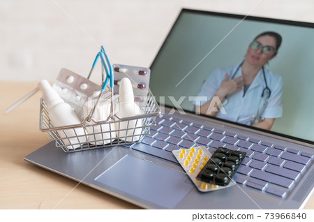 Video conference with a doctor on a laptop and tablet in a small shopping basket. Online pharmacy. Pharmacist on a computer screen. Video conference with a doctor on a laptop and tablet in a small shopping basket. Online pharmacy. Pharmacist on a computer screen. 73966840