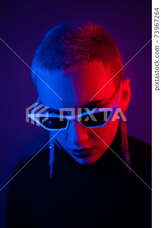 Portrait of a young woman with a short male haircut in sunglasses in neon light in the studio 73967264