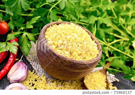 Bulgur in bowl with vegetables on dark wooden board 73968137