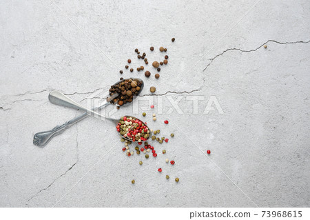 Two crossed spoons with different kinds of pepper 73968615