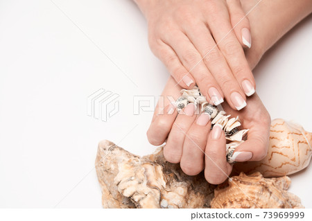 Beautiful Female well-groomed Hands with French manicure holding sea shell over light background 73969999