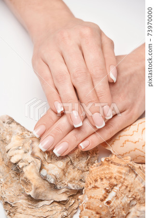Beautiful Female well-groomed Hands with French manicure holding sea shell over light background 73970000