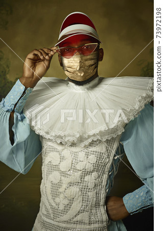 Portrait of medieval young man in vintage clothing and golden face mask on dark background. 73972198
