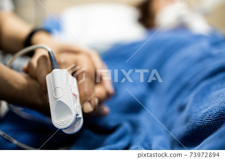 Asian patient's hand with an attached pulse oximeter on finger for monitoring,daughter holding her mother's hand,supporting comforting of seriously ill patient,intensive care in ICU room at hospital Asian patient's hand with an attached pulse oximeter on finger for monitoring,daughter holding her mother's hand,supporting comforting of seriously ill patient,intensive care in ICU room at hospital 73972894