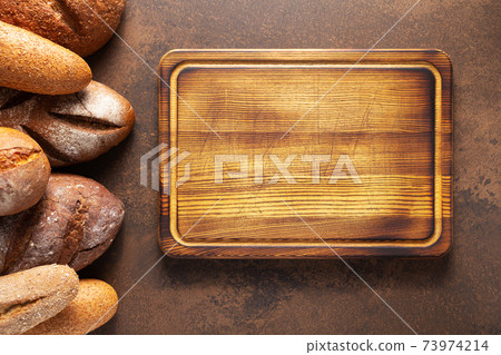 Loaf of fresh bread and buns with wooden cutting board on table 73974214