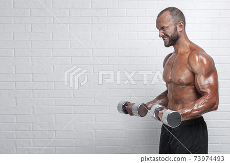 Bodybuilder doing exercises for biceps with a dumbbells against brick wall 73974493