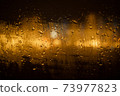 View of the night city through the wet car window with drops 73977823