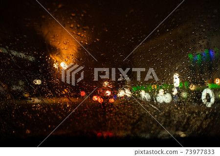 View of the night city through the wet car window with drops 73977833
