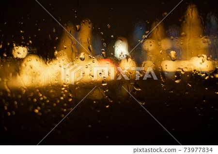 View of the night city through the wet car window with drops 73977834
