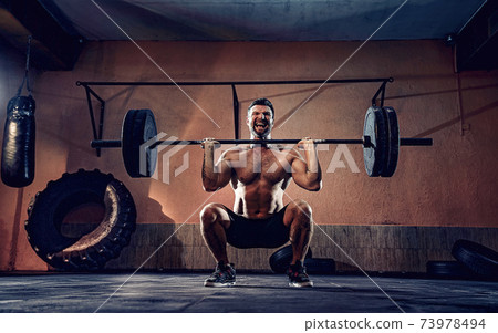Muscular fitness man doing push a barbell over his head in his garage, selfisolation. Functional training. Snatch exercise Muscular fitness man doing push a barbell over his head in his garage, selfisolation. Functional training. Snatch exercise 73978494