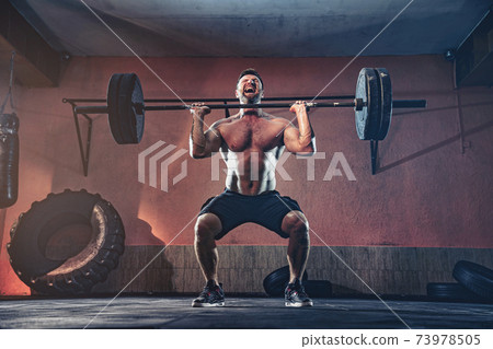 Muscular fitness man doing push a barbell over his head in his garage, selfisolation. Functional training. Snatch exercise Muscular fitness man doing push a barbell over his head in his garage, selfisolation. Functional training. Snatch exercise 73978505