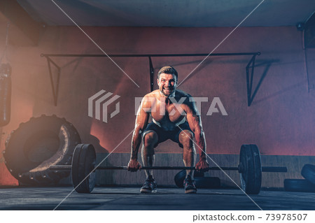 Muscular fitness man doing push a barbell over his head in his garage, selfisolation. Functional training. Snatch exercise Muscular fitness man doing push a barbell over his head in his garage, selfisolation. Functional training. Snatch exercise 73978507