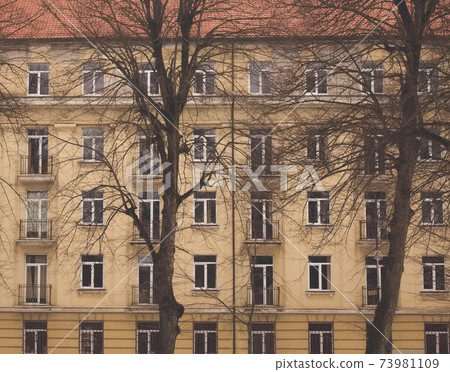 A part of yellow brown building facade with windows and a tree in front of it. Street view cityscape of Klaipeda city in Litrhuania. Retro hipster faded style of processing. Grey and gloomy mood A part of yellow brown building facade with windows and a tree in front of it. Street view cityscape of Klaipeda city in Litrhuania. Retro hipster faded style of processing. Grey and gloomy mood 73981109