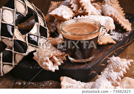 Carnival food TYPICAL, mask and aromatic coffee on a woody background. Sfrappole or chiachiere or 73982825