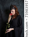 Woman in black dress sniffs red rose 73983957