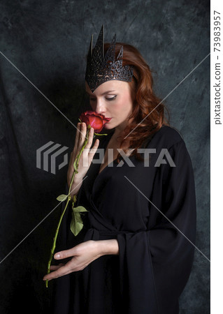 Woman in black dress sniffs red rose 73983957