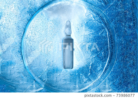glass frozen ampoule with a virus vaccine on the texture of cold ice top view, background with backlight on the theme of pharmaceutical drugs from viral diseases. 73986077