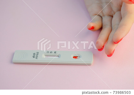 test for coronavirus lies on a pink background. there is a drop of blood on the test strip. express diagnostics of coronavirus. home test to diagnose infection. next to the girl's hand with red test for coronavirus lies on a pink background. there is a drop of blood on the test strip. express diagnostics of coronavirus. home test to diagnose infection. next to the girl's hand with red 73986503